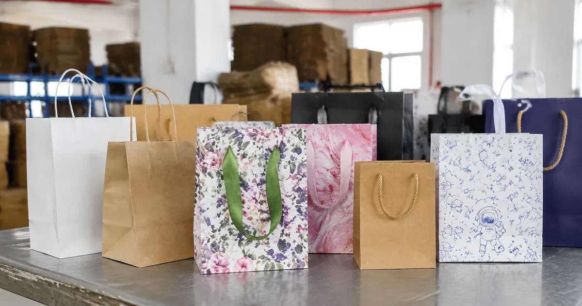 Custom printed paper gift bags with logos and handle options arranged on a factory inspection table